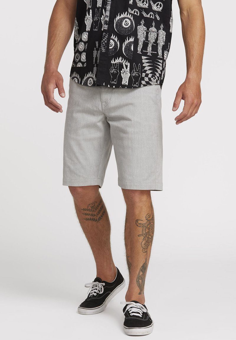 Light gray shorts in a relaxed fit, made from a smooth fabric, with side pockets and rolled hems, paired with a patterned black shirt.