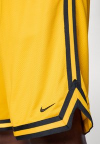 Gule Nike-shorts med sorte accenter, der har en mesh-struktur, sidelister og et lille logo ved kanten.