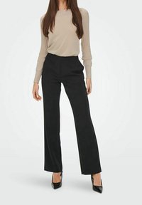 Beige geribd lang mouw shirt gecombineerd met hooggetailleerde zwarte wijde broekspijpen en zwarte hakken, met de nadruk op gladde texturen en neutrale kleuren.