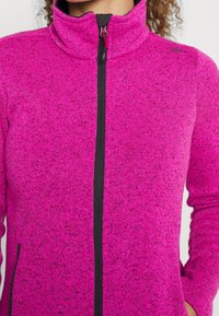 Giacca in pile con zip di colore rosa brillante, colletto alto, zip nera e tasche laterali. Tessuto a maglia testurizzato con un motivo spruzzato.