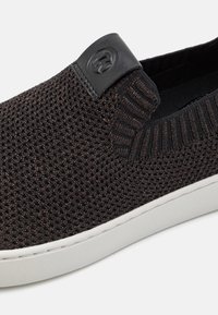 Chaussure noire tricotée à enfiler avec semelle blanche et petite languette en cuir noir avec logo circulaire embossé.
