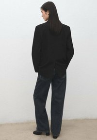 Blazer negro de corte entallado, con una sola abertura trasera, combinado con vaqueros de mezclilla oscura y corte holgado. Tejido liso con detalles mínimos.