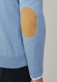 Jasnoniebieski sweter z prążkowanym dołem i mankietami, z beżowymi zamszowymi łaty na łokciach. Gładka faktura i dopasowany krój.