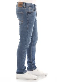 Slim-fit niebieskie dżinsy o średnim praniu, z pięcioma kieszeniami, kontrastowym przeszyciem i brązową skórzaną łatą na pasku.