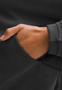 Dark hoodie featuring a hand in a side pocket. The material is smooth with a subtle texture, and the cuffs have a ribbed finish.