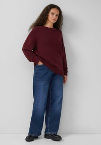Bordeaux chunky gebreide trui met een brede halslijn, gecombineerd met losse donkerblauwe jeans en zwarte enkellaarsjes.