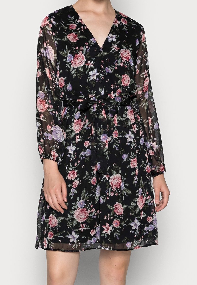Robe florale en tissu transparent noir, ornée de roses et de fleurs violettes. Design en V, manches longues et taille cintrée à nouer.