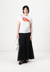 Camiseta branca com estampa de lagosta vermelha, combinada com uma saia maxi preta em camadas. Inclui uma pequena bolsa branca e sapatilhas pretas.