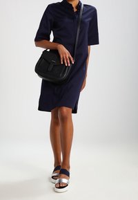 Mörkblå skjortklänning med korta ärmar, krage och rak passform. Samlad med en svart axelväska och klumpiga vita sandaler med mörkblå remmar.