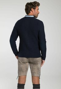 Marineblauwe gebreide trui met een gestructureerde achterkant, ronde halslijn en geribde boorden, gecombineerd met grijze shorts met blauwe kantaccenten.