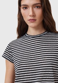 T-shirt à manches courtes noir et blanc à rayures avec un col rond. Le tissu semble léger et légèrement transparent avec une finition texturée.