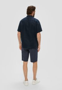 Donkerblauw kortebloes met een ontspannen pasvorm, gecombineerd met marineblauwe gestreepte shorts. De outfit wordt aangevuld met witte sneakers.