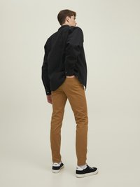 Czarna koszula na guziki, beżowe slim-fit spodnie, czarne sneakersy z białymi podeszwami, stojący na tle jasnym. Prosty i casualowy design.