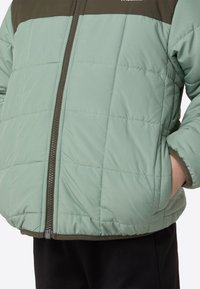 Heleroheline puffer-jope pruuni ülaosaga, millel on tikitud muster, esimesel küljel lukk ja küljetaskud.