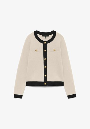 Cardigan beige avec un col et des poignets côtelés noirs, doté de deux poches à rabat et de boutons dorés sur le devant. Texture en tricot douce.