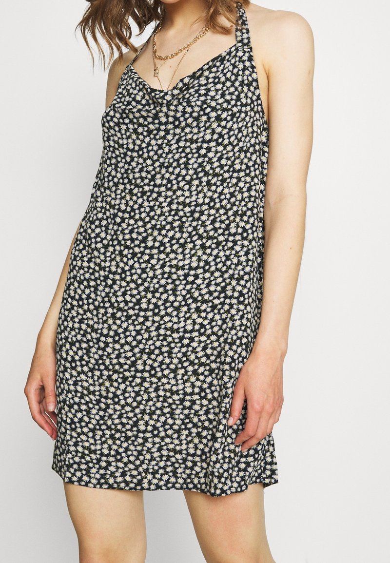 Robe noire sans manches avec un motif de marguerites blanches, dotée de fines bretelles et d'une coupe décontractée. Tissu léger avec une texture lisse.