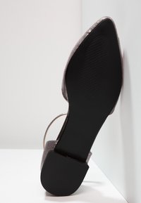 Chaussure à talon haut scintillante grise avec un bout pointu et une semelle en caoutchouc noire, dotée d'une bride transparente à la cheville et d'une texture lisse.