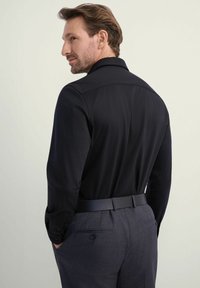 Czarna koszula z długim rękawem i standardowym kołnierzykiem, sparowana z szarymi spodniami o teksturowanej fakturze i czarnym paskiem, uchwycona z tyłu.