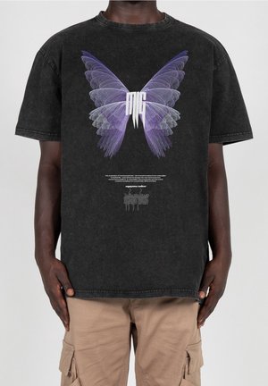 Black t-shirt with large purple butterfly wings graphic and white stylized letters "MG" in center, worn by person with beige cargo pants.