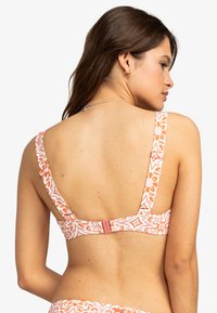 Hnedo-biely bikiny top s kvetinovým vzorom, so širokými ramienkami a zapínaním na háčik na zadnej strane s hladkým povrchom.