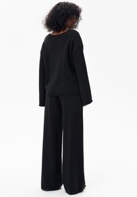Czarny dziany sweter i spodnie o szerokich nogawkach, charakteryzujące się luźnym krojem, opuszczonymi ramionami oraz prążkowanymi ściągaczami, ukazujące miękką fakturę i gładkie wykończenie.