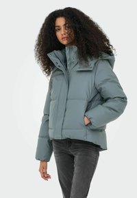 Chaqueta acolchada en un verde azulado apagado con un alto cuello, cierre de cremallera y botones a presión. Presenta bolsillos laterales y un corte corto y amplio.