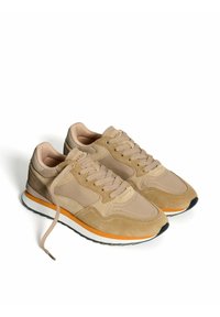 Zapatillas deportivas beige con materiales de ante y textil, con una entresuela naranja, punta redonda y suela gris. Los cordones están colocados de forma central.