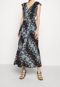 Blommig omlottklänning i svart, med volangärmar, V-ringning och knytmidja. Ljusrosa och gröna blommönster pryder tyget.