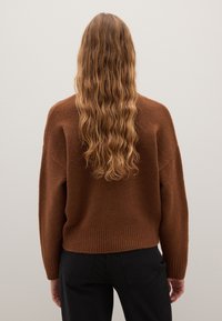 Maglione marrone lavorato a maglia con una vestibilità ampia, orlo a coste e maniche lunghe. Texture morbida, indossato con pantaloni neri, visto da dietro.