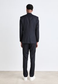 Traje azul marino ajustado con un blazer estructurado y pantalones a juego, combinado con zapatillas blancas. Tejido suave y mate con una silueta limpia.
