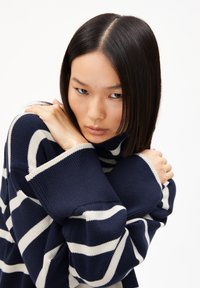 Pull en tricot épais bleu marine avec des rayures horizontales crème. Doté d'un col haut et de manches surdimensionnées, mettant en valeur un motif de tricot texturé.