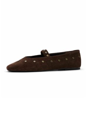 Bruine suède platte schoen met ronde metalen studs en een klein bandje over de bovenkant, zijaanzicht op een witte achtergrond.
