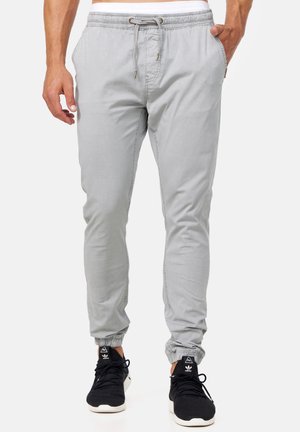 Mann trägt hellgraue Jogginghosen mit Kordelzug in der Taille und elastischen Bündchen, kombiniert mit schwarzen Adidas-Sneakern.