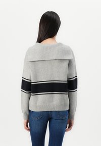Pull gris clair avec des rayures noires, poignets côtelés et col rabattu. Présente une texture douce et un ourlet droit. Porté sur un jean bleu foncé.
