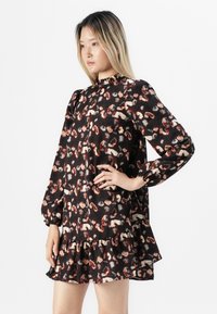 Robe noire avec un ourlet en volants et de longues manches bouffantes, présentant un motif abstrait coloré dans des teintes de rouge, beige et gris.