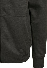 Felpa con zip di colore grigio scuro, caratterizzata da una texture morbida, tasche frontali e un'etichetta all'orlo. I polsini sono aderenti per una vestibilità comoda.