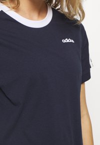 Camiseta de algodón azul marino con ribete blanco en el cuello redondo. Presenta un pequeño logo blanco de Adidas en el pecho y un diseño sutil en las mangas.