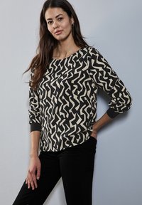 Blusa de manga larga en negro y crema con un patrón de zigzag. Presenta un escote redondo y puños elásticos. Está confeccionada con una tela suave y ligera.
