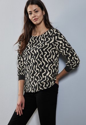 Chemisier à manches longues noir et crème avec un motif en zigzag. Présente un col rond et des poignets élastiques. Fabriqué en tissu léger et doux.