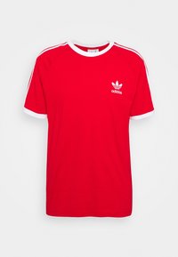 Camiseta de algodón roja con acentos blancos, cuello redondo y mangas cortas tipo raglán. Presenta un pequeño logotipo de Adidas en blanco en el pecho.
