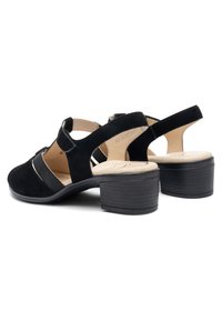 Sandalias negras de ante con tacón bajo y ancho, con correa ajustable y parte trasera abierta, cuentan con plantillas acolchadas beige para mayor comodidad.