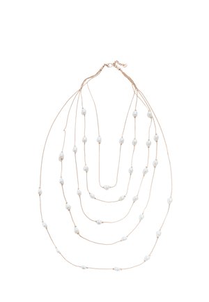 Long collier à chaînes multiples en or avec des perles blanches espacées de manière irrégulière sur fond blanc.
