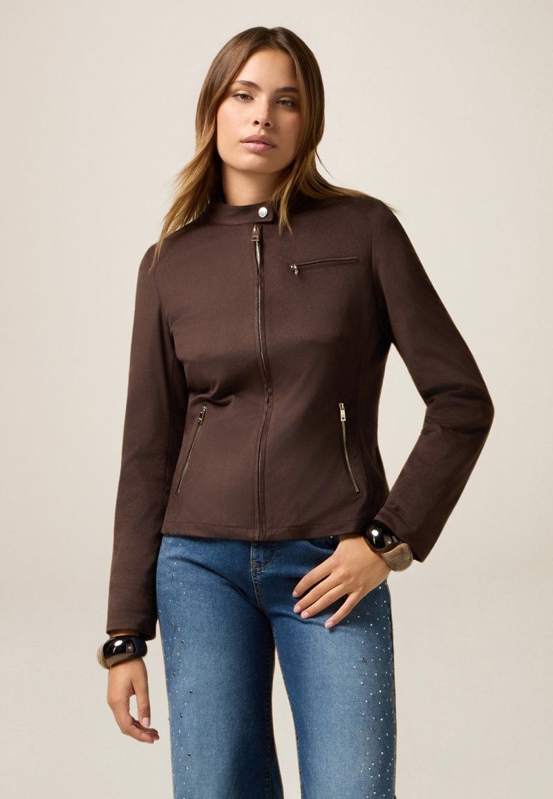 Veste marron zippée avec un col montant, poches latérales zippées et une poche poitrine. Texture lisse avec un matériel minimal et un design ajusté.