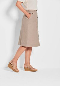 Knee-lange braune Leinenrock mit Knopfleiste, elastischem Bund und seitlichen Taschen. Kombiniert mit hellbraunen Keilsandaletten.