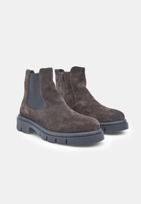 Botine din suede maro, cu panouri elastice laterale, vârf rotund și o talpă groasă din cauciuc negru. Prezintă detalii de cusătură pe margini.