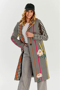 Płaszcz w wzór houndstooth z wielokolorowymi pionowymi paskami i kwiatowymi akcentami. Wykonany z tkaniny o gładkiej fakturze; z zapięciem na guziki.