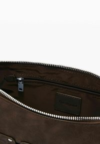 Braun gemusterter Handtaschen-Innenraum mit einem Reißverschlussfach und silbernem Reißverschluss. Verfügt über ein schwarzes Etikett mit dem Text "Desigual". Glatte Stoffoberfläche.