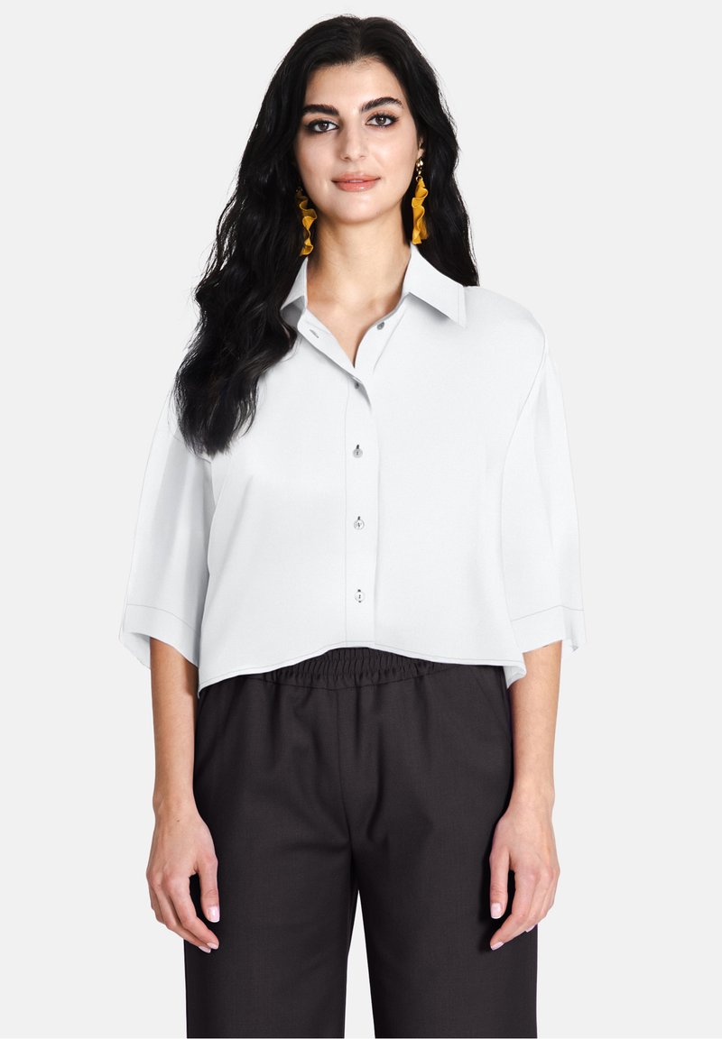 Camicia bianca cropped con colletto e maniche corte, abbinata a pantaloni scuri a vita alta. Tessuto liscio e vestibilità comoda.