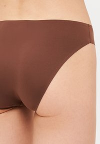 Bruine bikini-broekjes van een gladde stof, met een middelhoge snit en naadloze randen, die volledige bedekking op de achterkant bieden.