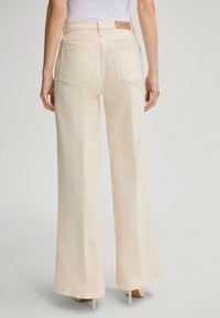 Jeans beige a gamba larga con una texture liscia e tasche posteriori. Presentano una vita con marchio e dettagli di cucitura sottili.
